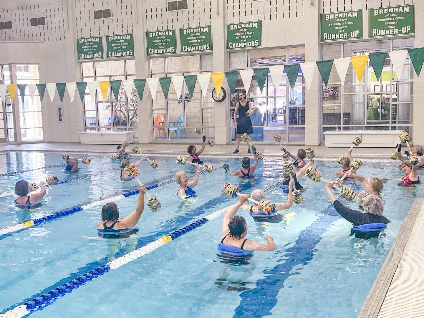 Aqua Cardio Class - a group of people lifting water weights in a large pool while listening to an instructor standing on the deck